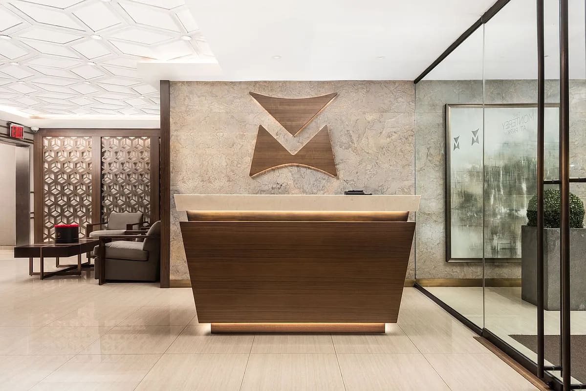 Modern lobby with curved wood reception desk, geometric wall sculpture, and glass partition dividing the space.