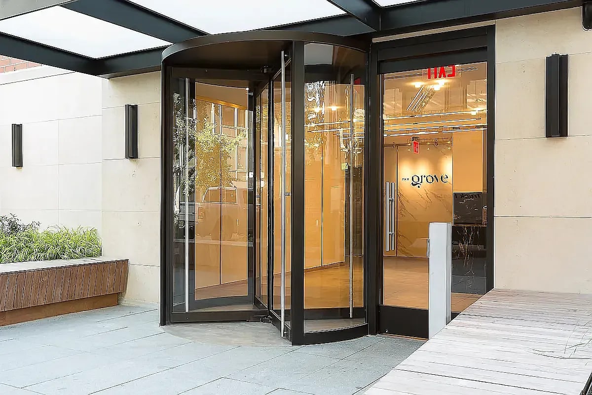 Modern building entrance with black-framed glass doors, warm wood flooring, and cream-colored exterior walls with integrated planters.