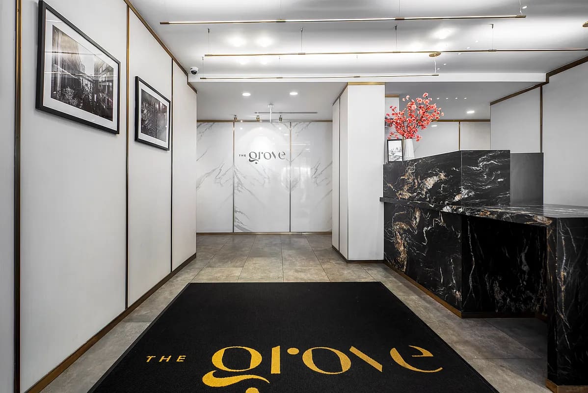 Modern building lobby with marble-clad walls, black stone reception desk with coral flowers, framed artwork, and brass-trimmed glass doors.