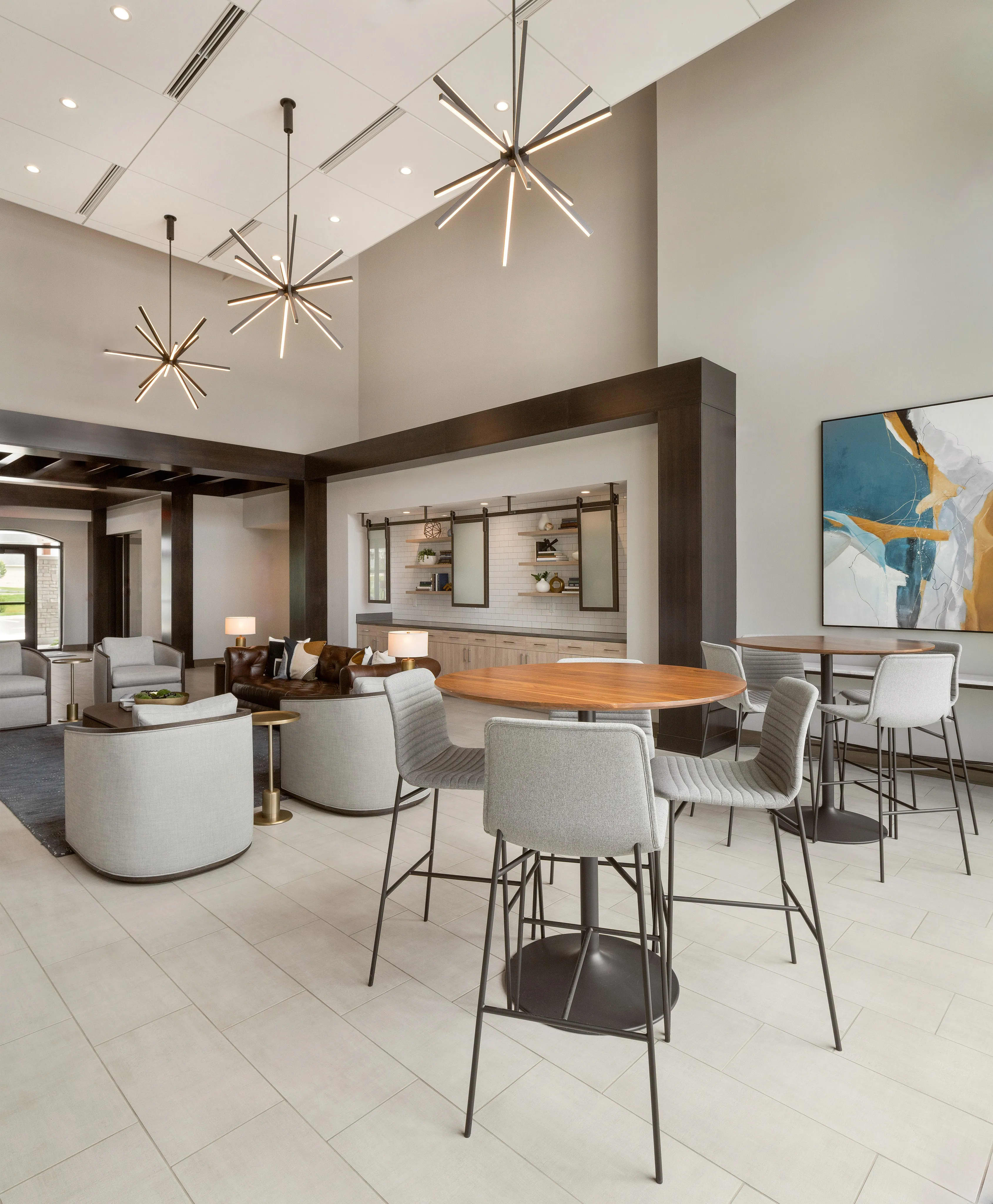Open-concept common area with vaulted ceiling, starburst pendant lights, wood dining table, gray upholstered bar stools, and built-in shelving.