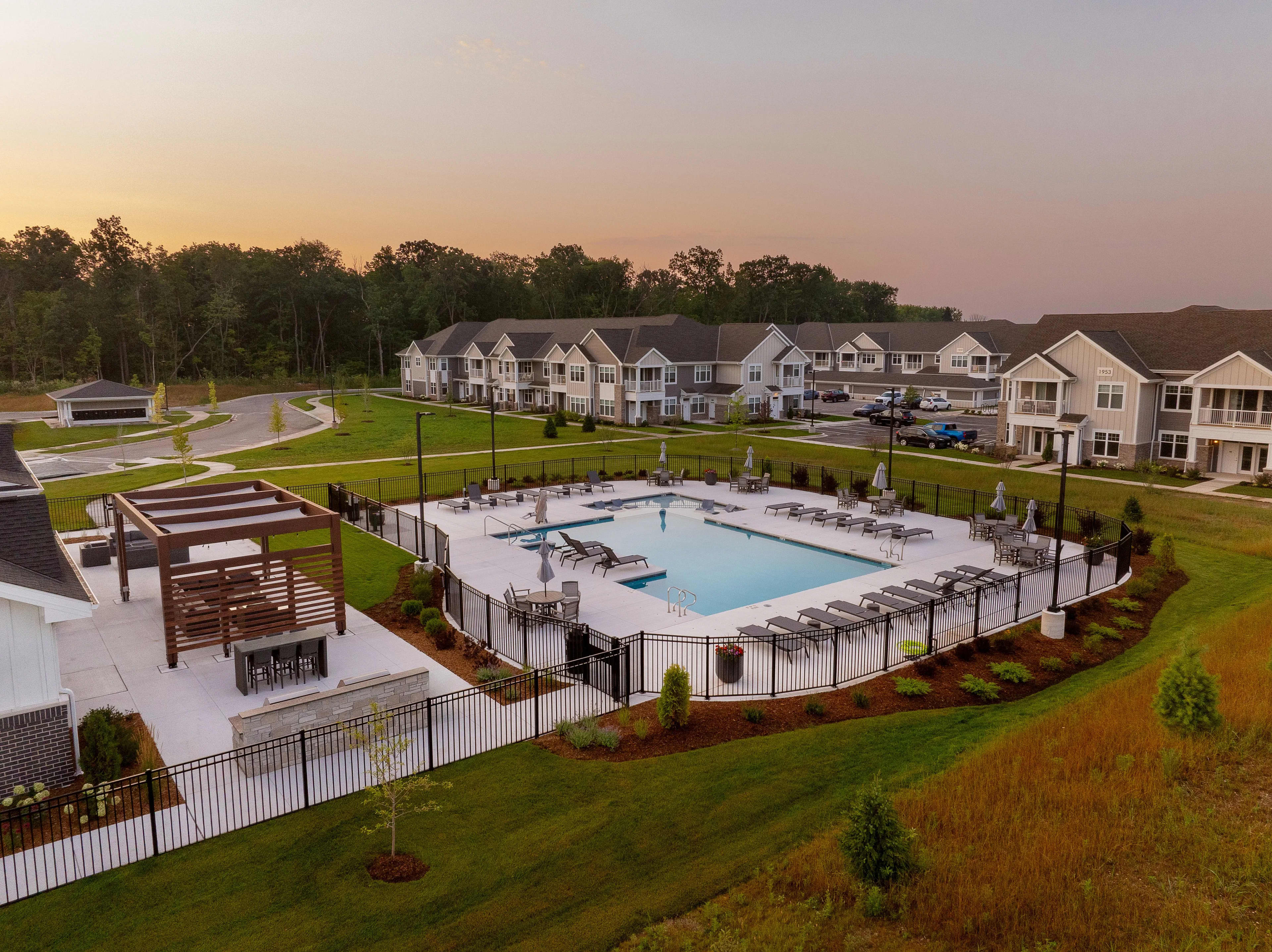 Resort-style swimming pool with lounge chairs, white fencing, and wooden cabana structure, surrounded by townhomes at sunset.