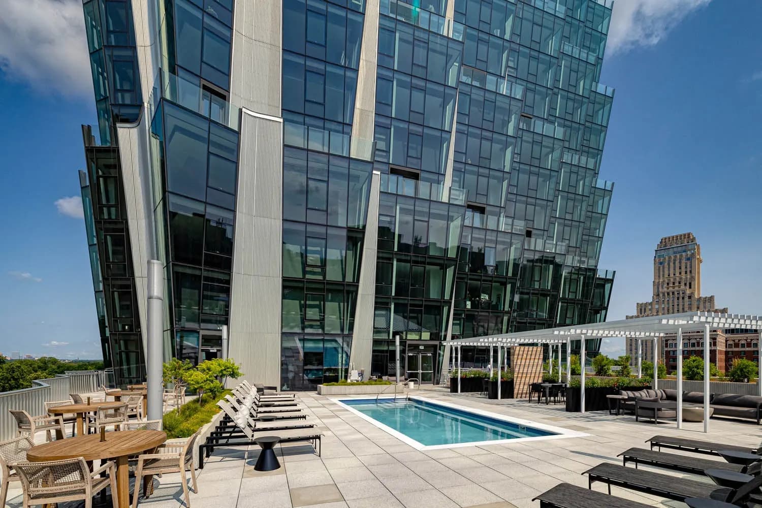 Rooftop pool deck with lounge chairs, dining tables, and modern glass building facade overlooking St. Louis skyline.