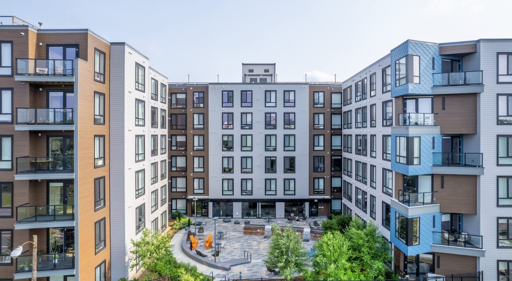 Central courtyard with paved plaza, orange seating, green trees, and surrounding multi-story apartment buildings with balconies.