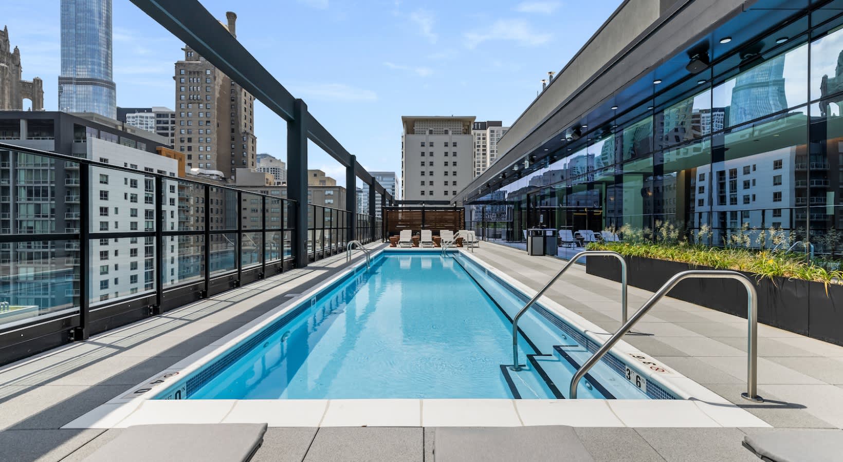 Rooftop swimming pool with black railings, lounge chairs, and downtown Chicago skyline in background.