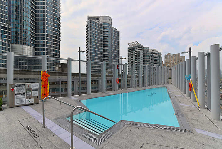 Rooftop swimming pool with bright turquoise water, metal railings, and surrounding high-rise residential towers in downtown Toronto.
