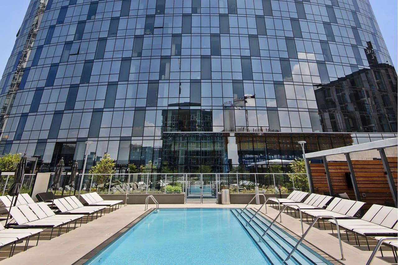 Rooftop swimming pool with blue water, metal lounge chairs, and a modern glass high-rise building backdrop.