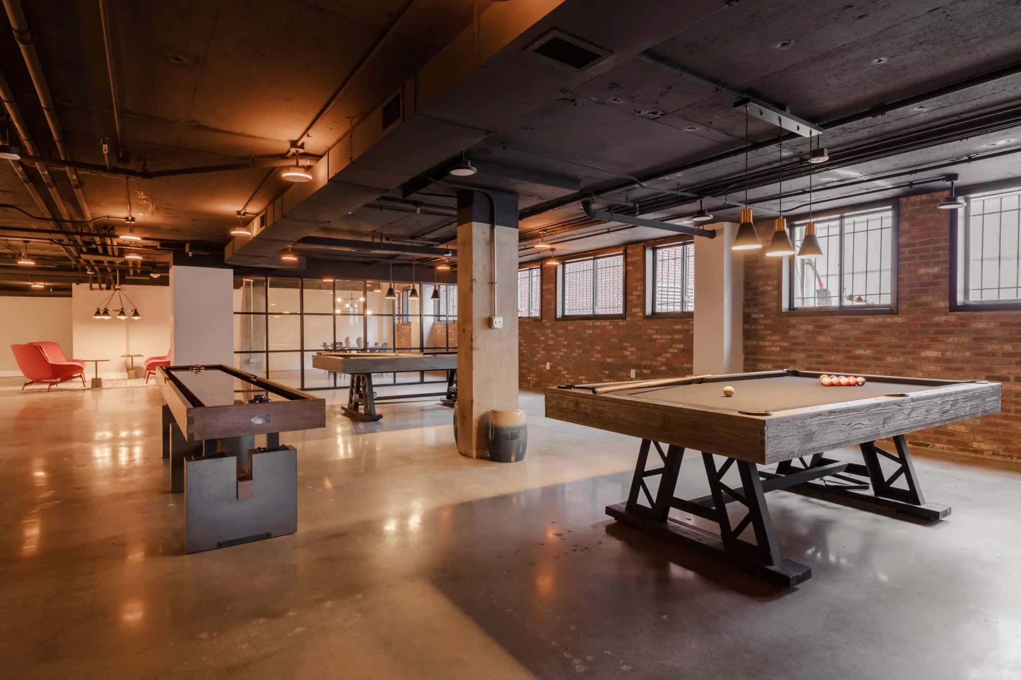 Recreation room with pool table, billiards table, exposed brick walls, concrete floors, and industrial ceiling with pendant lights.