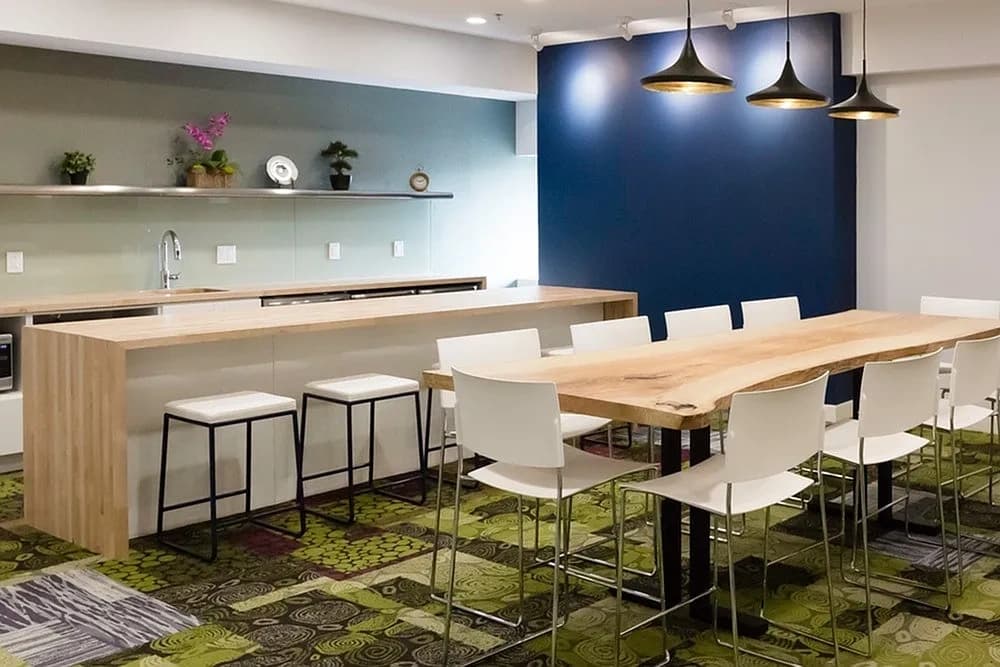 Open-concept kitchen and dining area with light wood island, white chairs, navy blue accent wall, and three black pendant lights.
