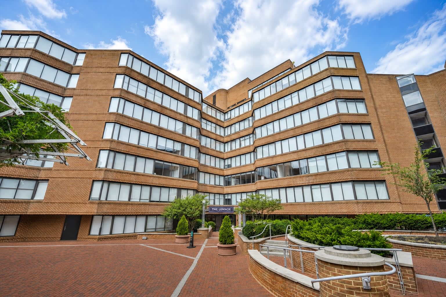 Multi-story brick residential building with horizontal window bands, curved architectural design, and landscaped courtyard with planters and seating areas.