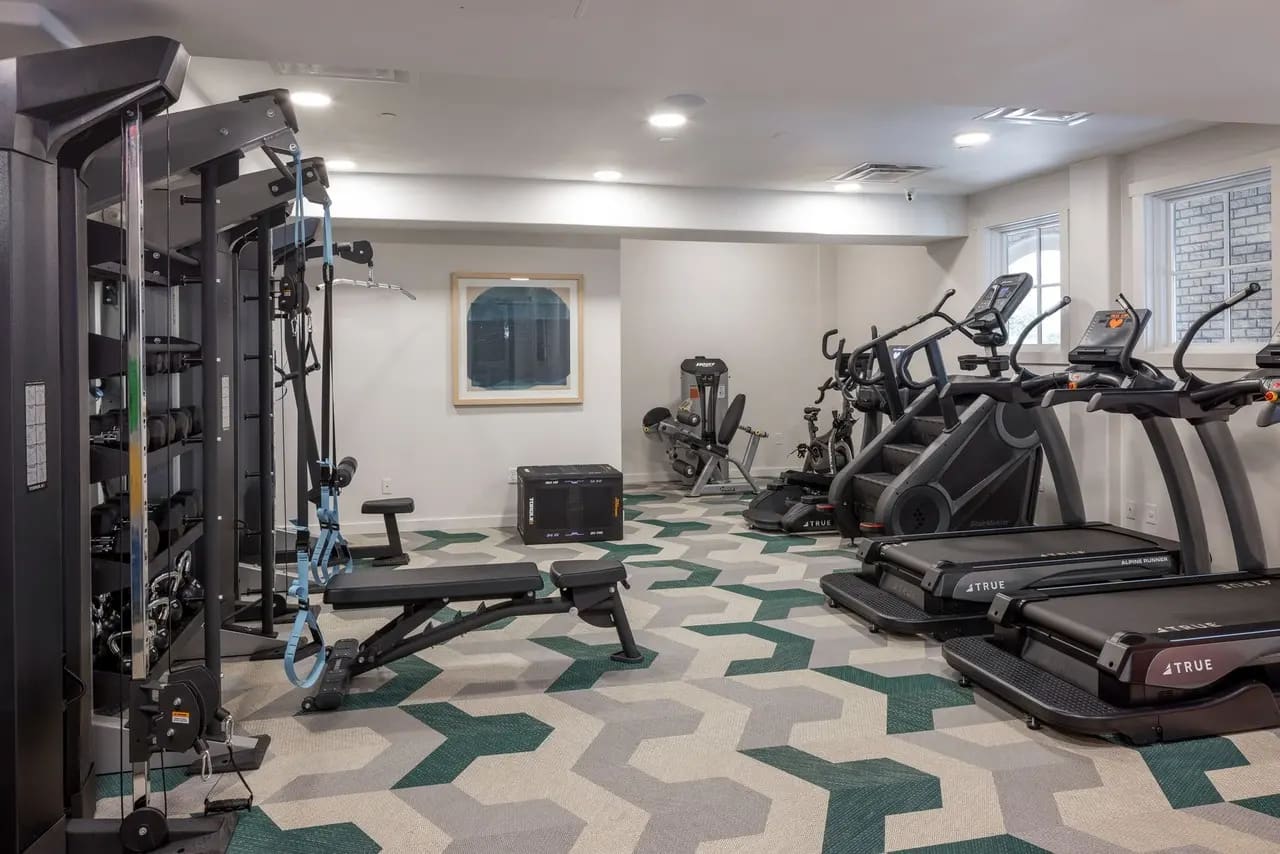 Modern fitness center with treadmills, stationary bikes, weight machines, and geometric green and beige floor pattern.