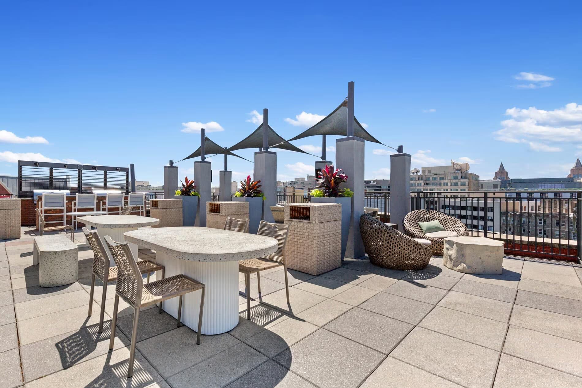 Rooftop terrace with oval dining table, woven lounge chair, black shade structures, and city views in Washington, DC.