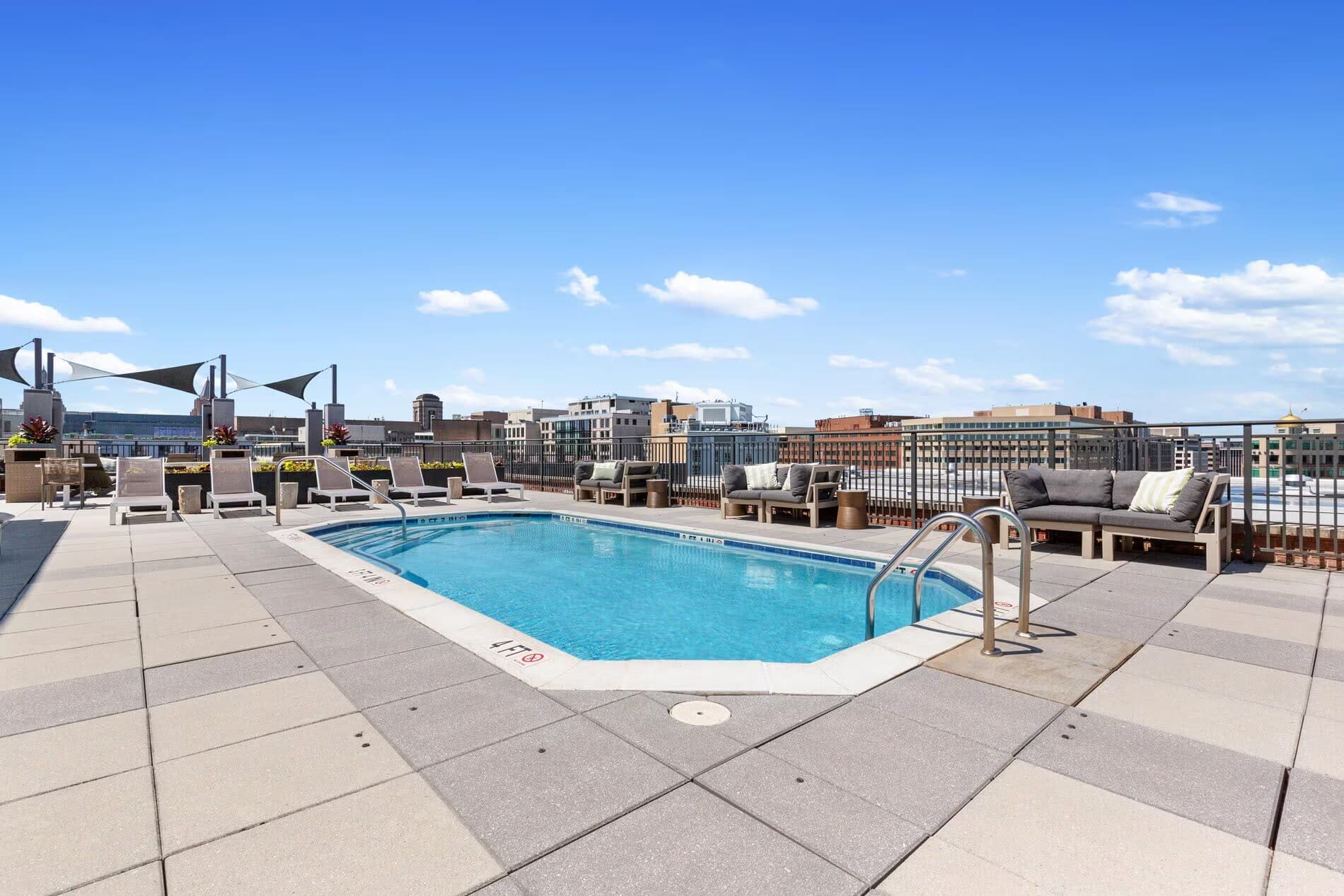 Rooftop pool with blue water, lounge chairs, shade structures, and downtown DC skyline views.