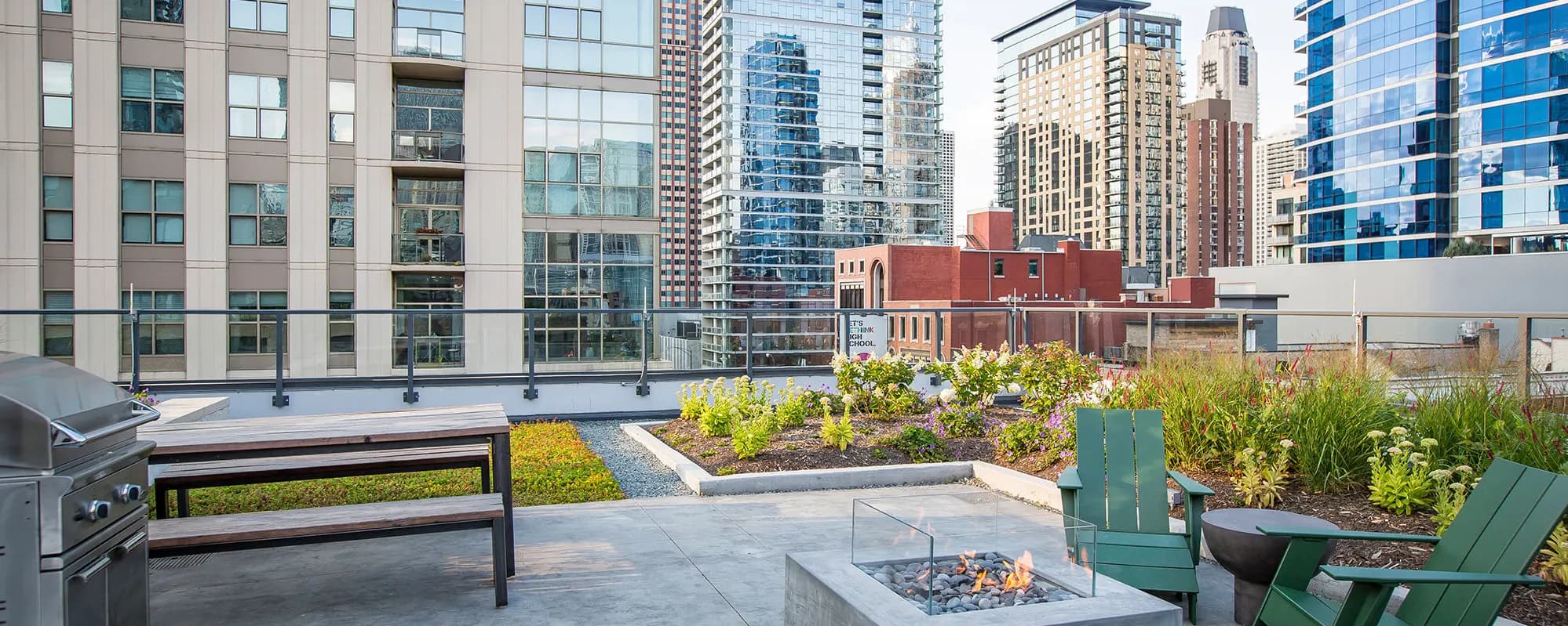 Rooftop terrace with fire pit, Adirondack chairs, planted gardens, and downtown Chicago skyline views.