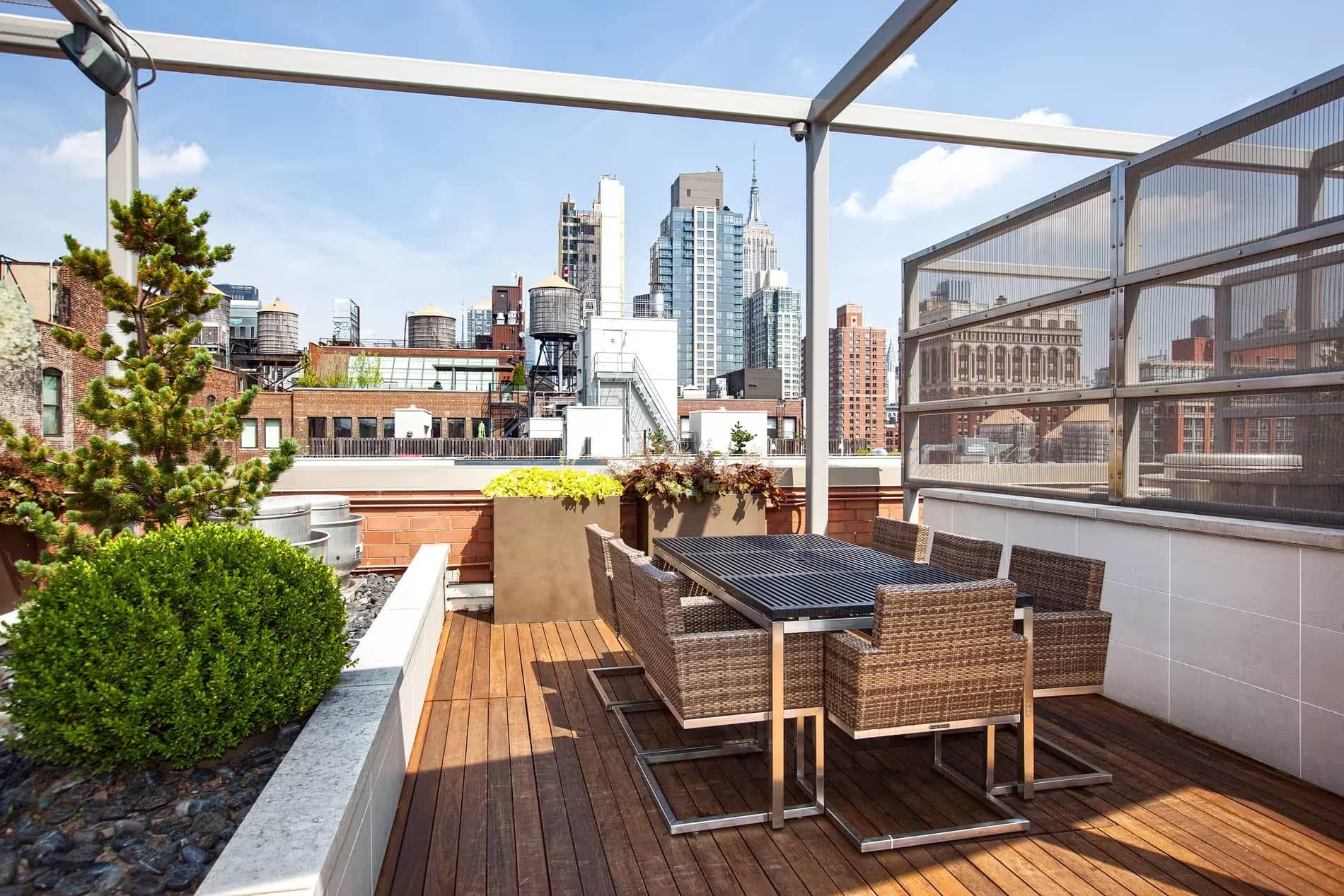 Rooftop terrace with woven dining chairs, wooden deck, potted plants, and Manhattan skyline views.