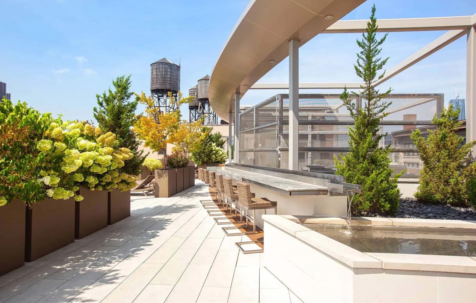 Rooftop terrace with wooden deck, potted trees, water features, pergola, and Manhattan skyline views.