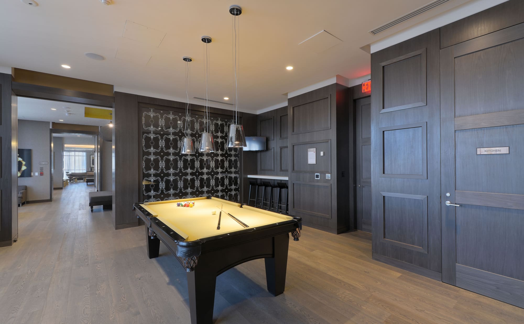 Game room with yellow felt pool table, black frame, pendant lights overhead, dark wood cabinetry, and geometric patterned accent wall.