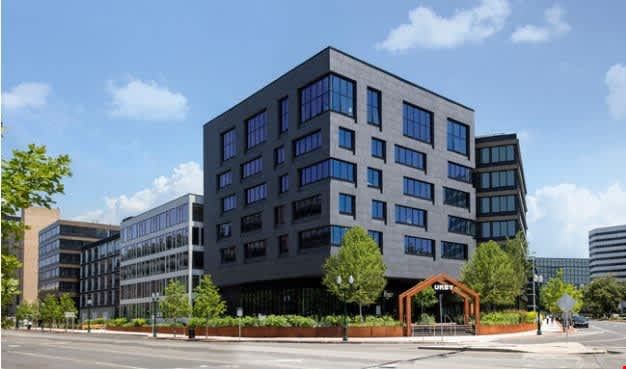 Modern multi-story apartment building with dark facade and blue-tinted windows, surrounded by landscaping and street-level retail space in downtown Stamford.