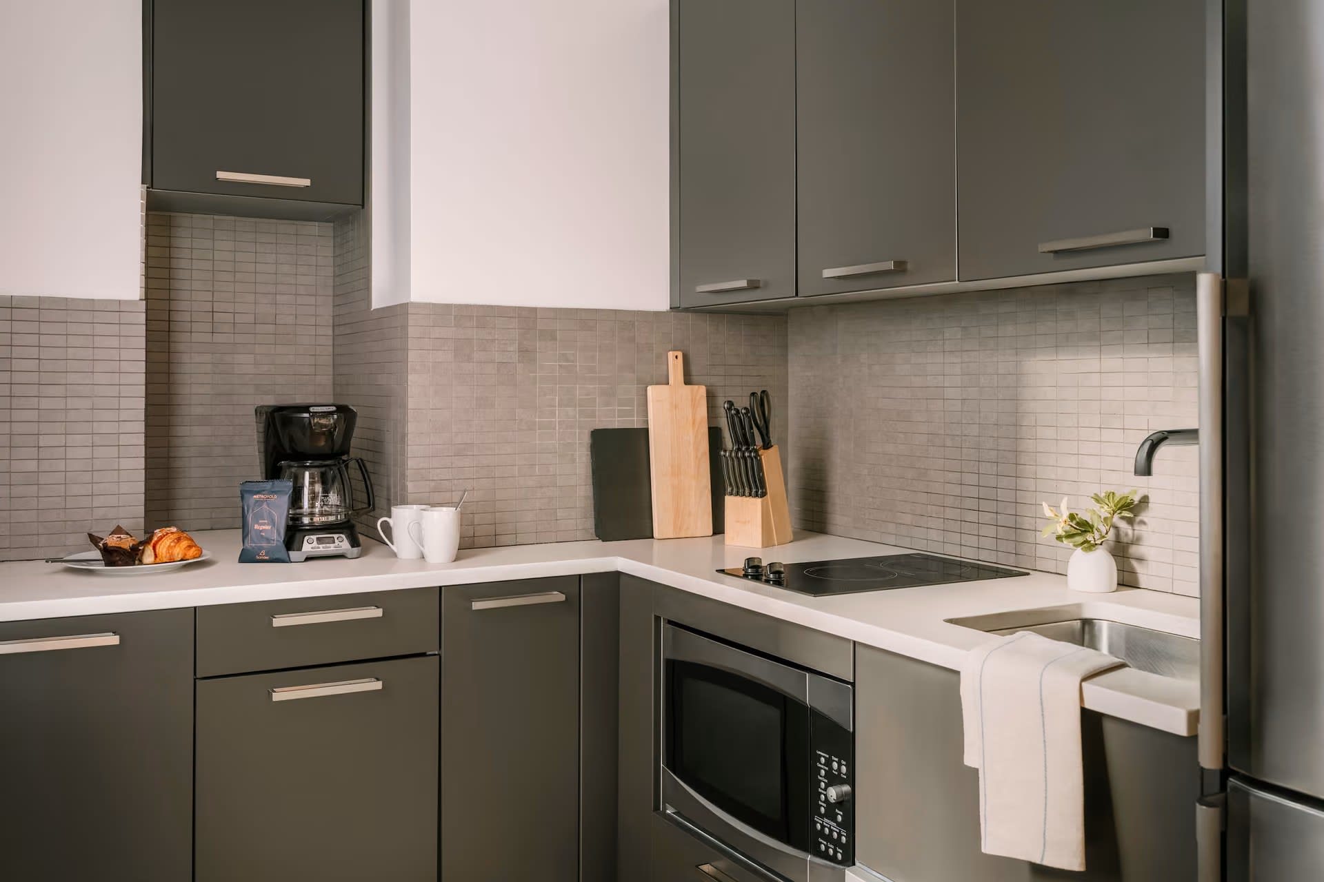 Modern kitchen with sage-green cabinets, white countertops, subway tile backsplash, and stainless steel appliances including microwave and cooktop.