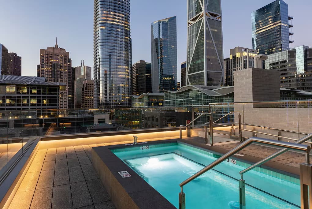 Rooftop pool and hot tub with illuminated deck overlooking San Francisco downtown skyline at dusk.