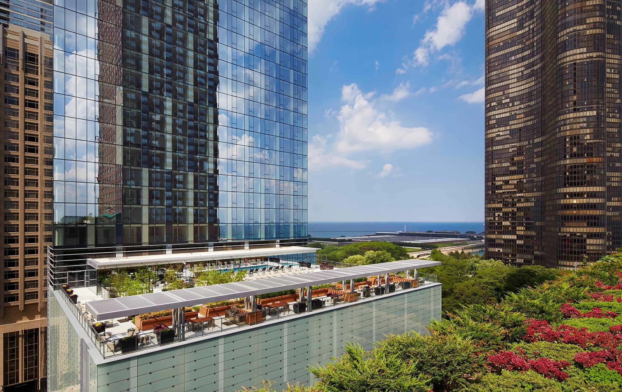 Rooftop terrace with dining area, green plantings, and views of Lake Michigan between high-rise buildings in Chicago.