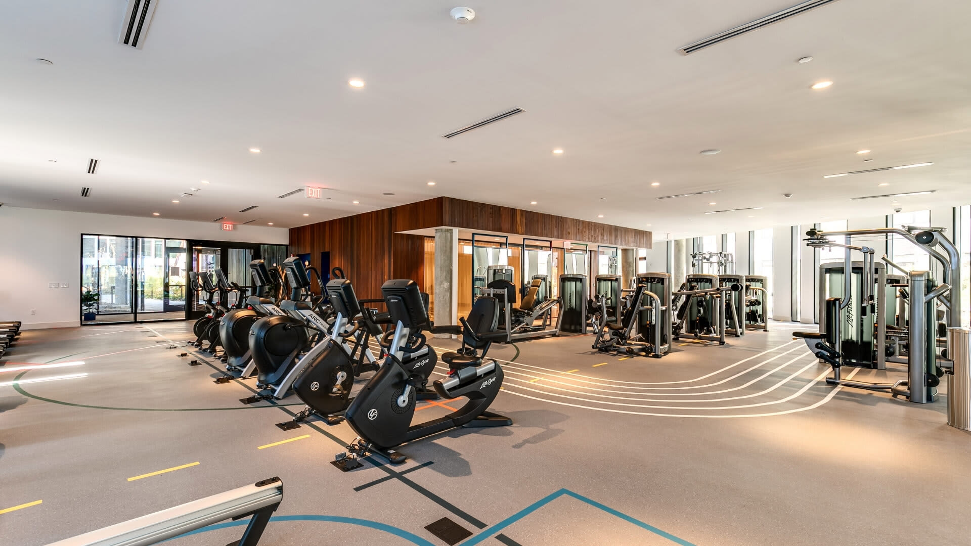 Modern fitness center with rows of stationary bikes, weight machines, and cardio equipment under recessed lighting.