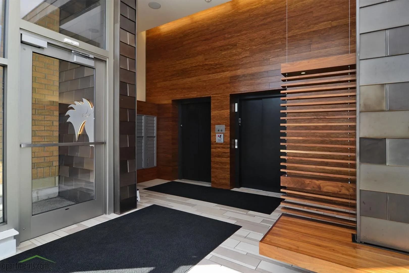 Building lobby with rich wood-slat accent wall, black entry doors, gray tile flooring, and glass entrance on left.