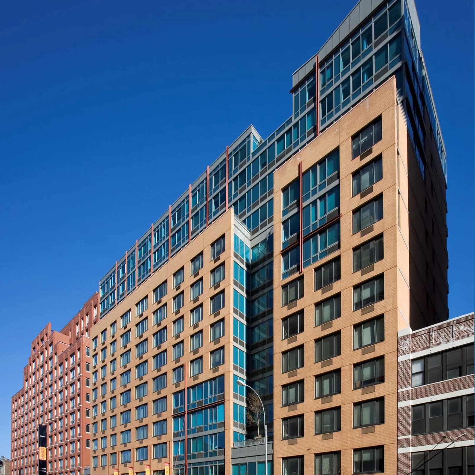 Multi-story residential building with tan brick and glass facade featuring rows of windows against clear blue sky.