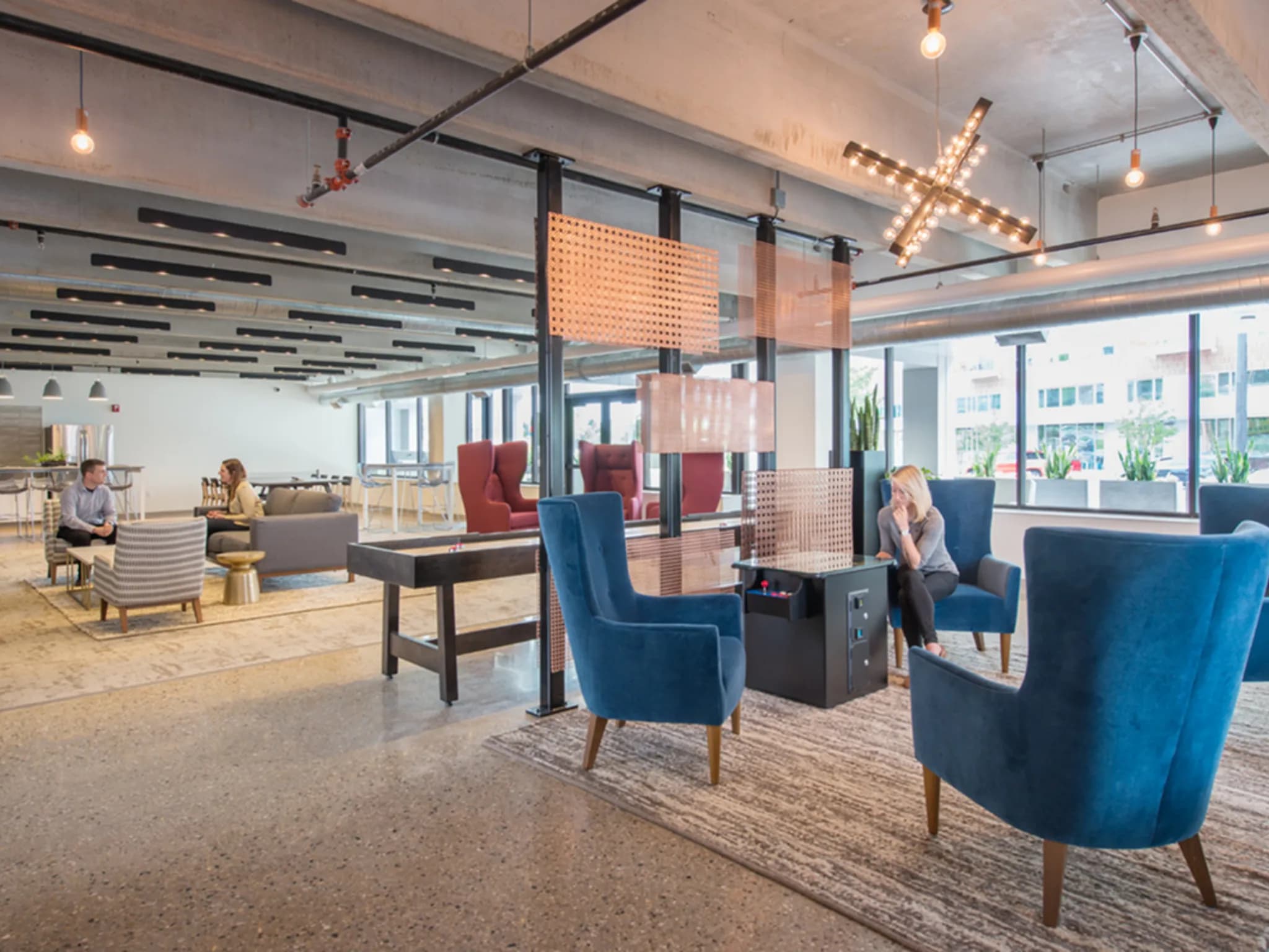 Open-concept lounge with blue upholstered chairs, black support columns, pendant lights, and city views through large windows.