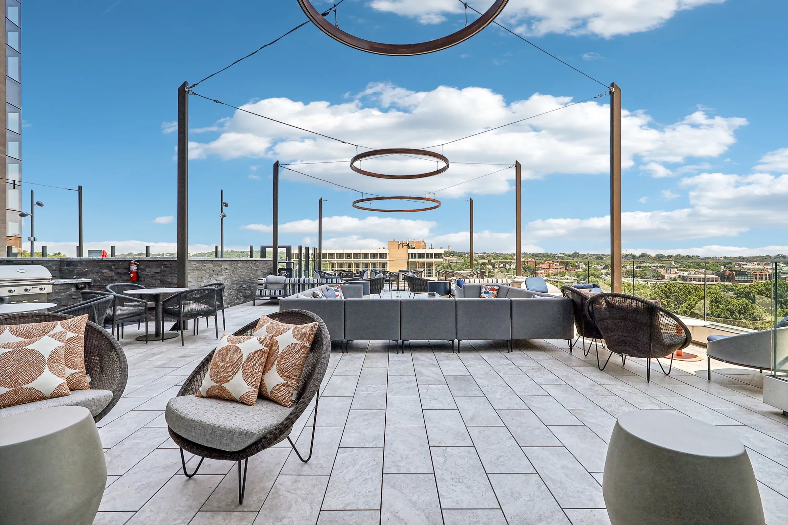 Rooftop terrace with modern woven chairs, circular hanging lights, gray pavers, and panoramic views of Arlington skyline.