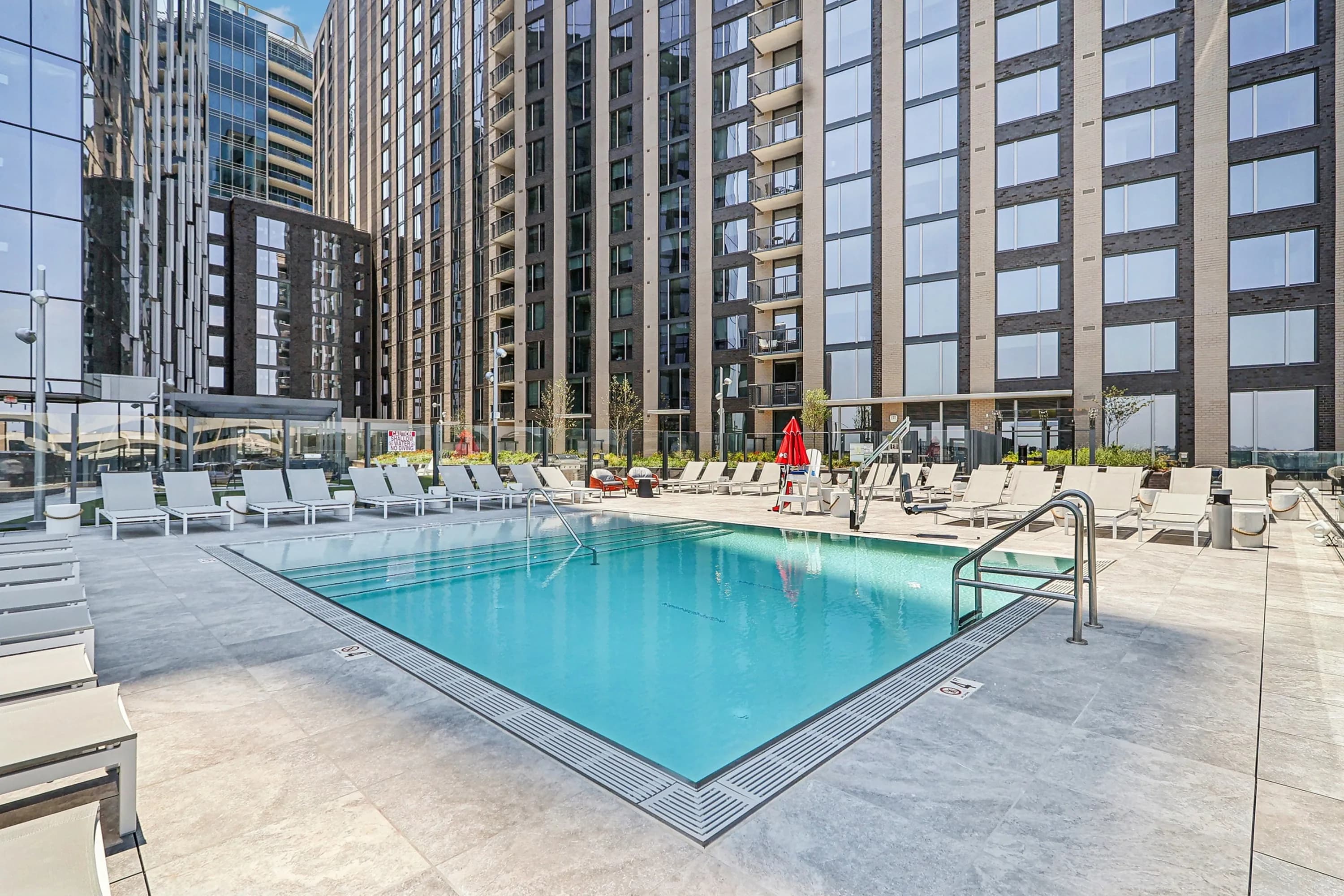 Outdoor swimming pool with clear blue water, surrounded by white lounge chairs and tall residential buildings in Arlington.