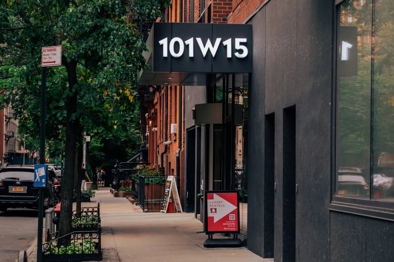 Modern black storefront with 101W15 signage on a tree-lined Manhattan street with brick buildings.