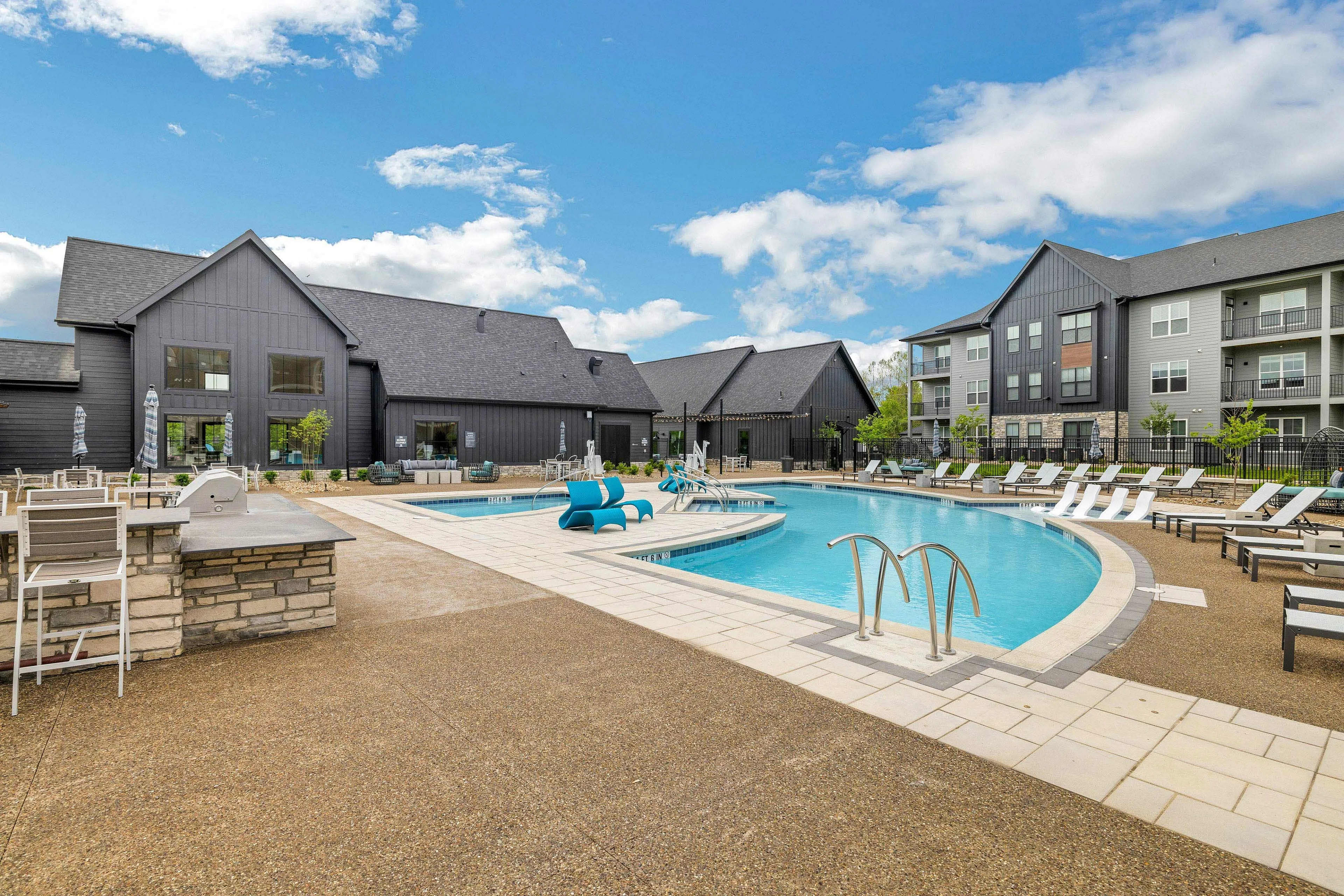 Resort-style swimming pool with blue water, lounge chairs, and modern black clubhouse buildings under clear sky.