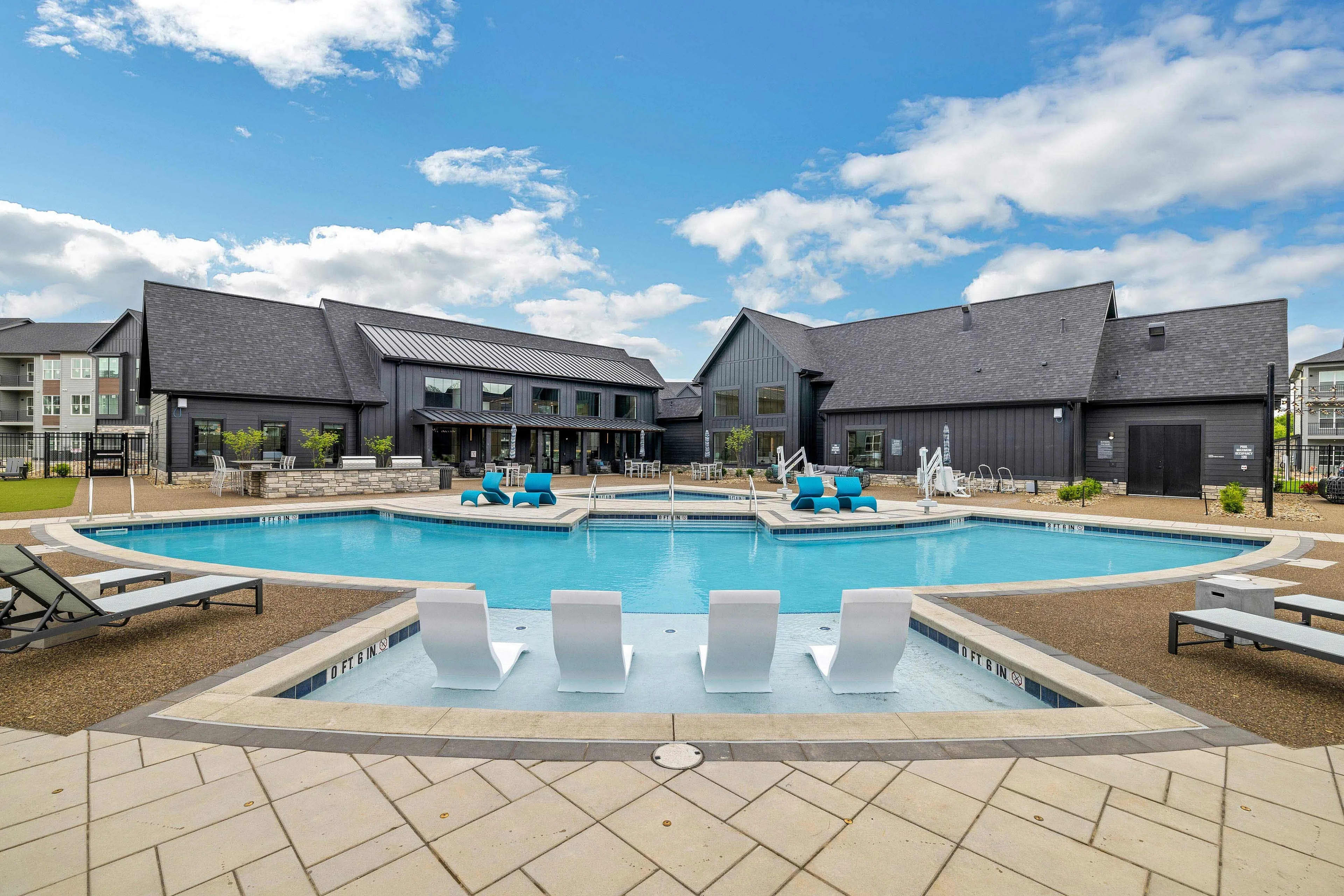 Resort-style swimming pool with spa tub, lounge chairs, and modern black residential buildings under blue sky.