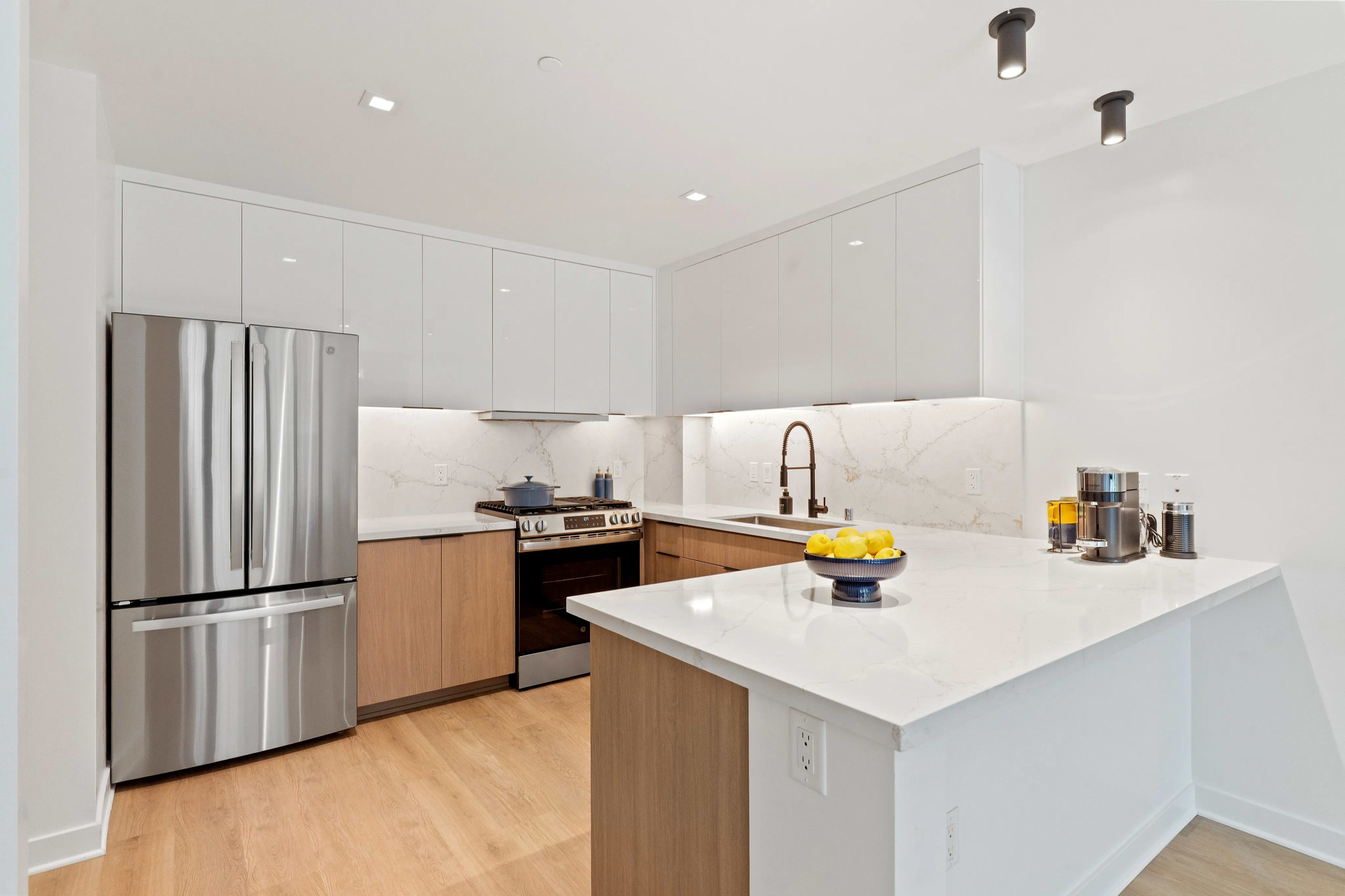 Contemporary kitchen with white upper cabinets, wood lower cabinets, stainless steel refrigerator and range, white marble countertops, and island with seating.