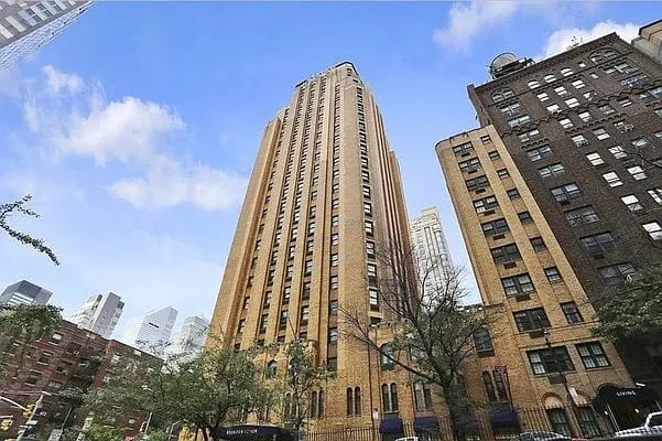 Tall Art Deco residential building with golden brick facade and vertical ribbing, flanked by other historic buildings under blue sky.