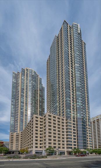 Modern residential high-rise towers in Jersey City with lower-rise building in foreground, blue sky background.