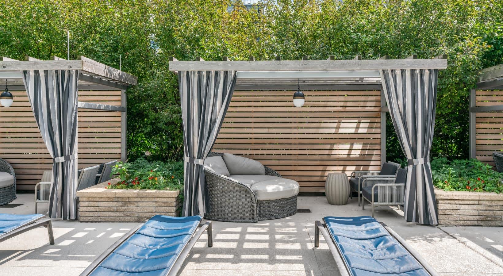 Outdoor courtyard with striped pergolas, gray wicker lounge chair, blue chaise lounges, and ivy-covered walls.