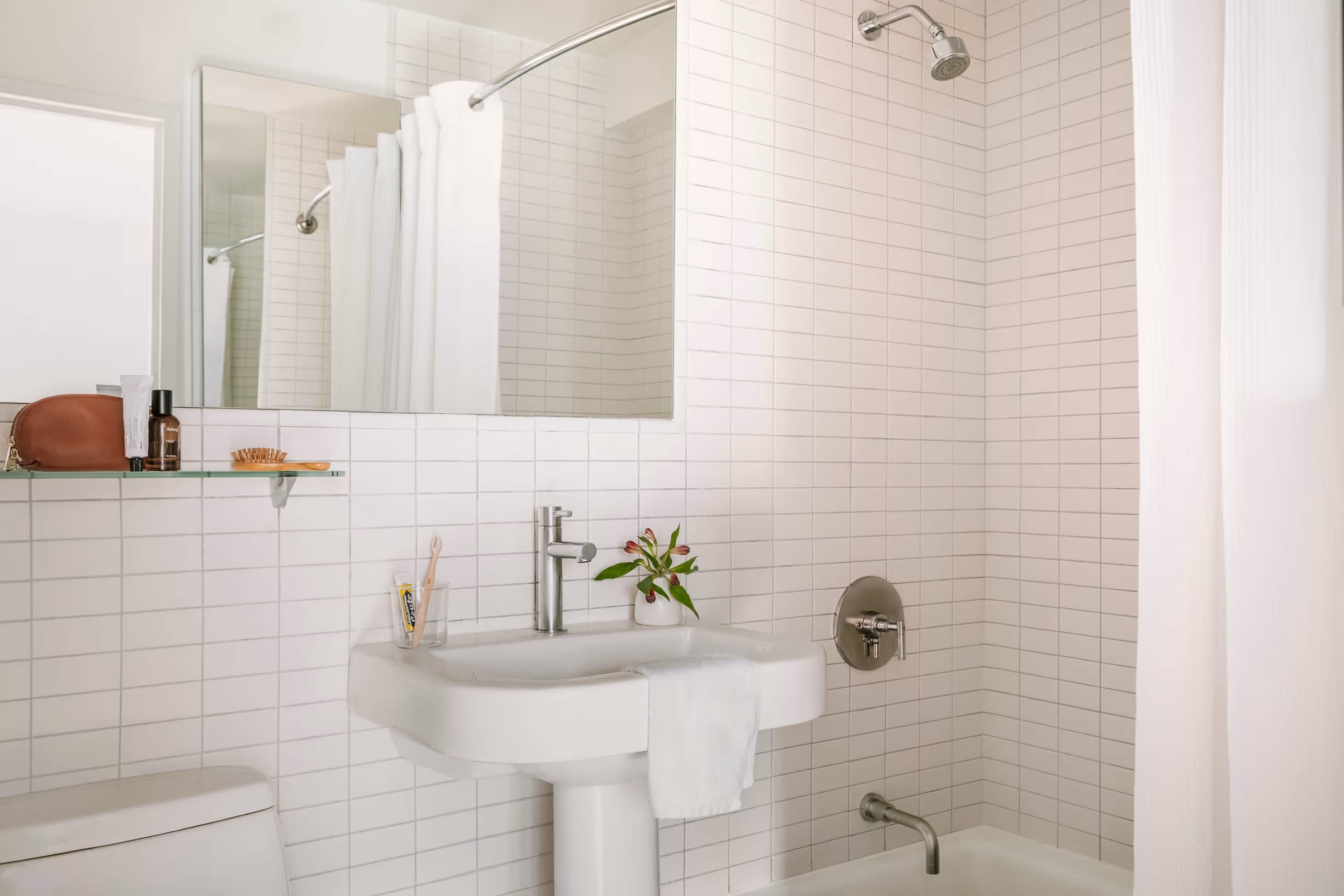 Bathroom with white subway tile walls, pedestal sink, large mirror, and glass shower enclosure with white curtain.