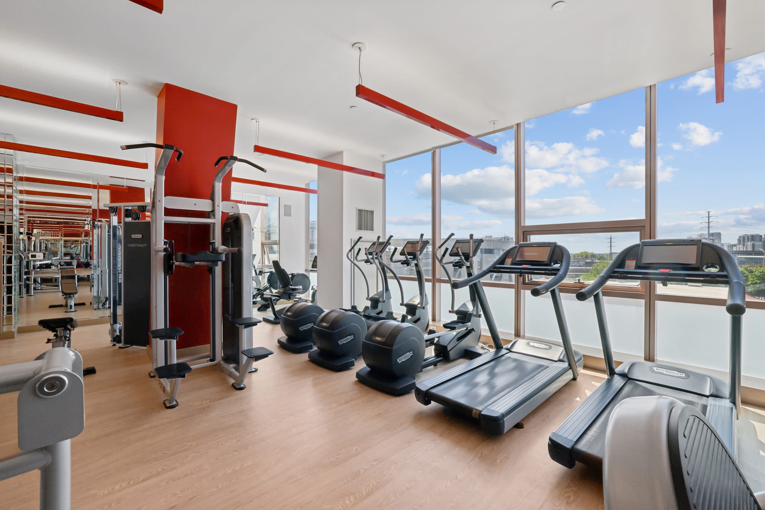 Fitness center with treadmills, ellipticals, and weight machines along floor-to-ceiling windows overlooking Stamford cityscape.