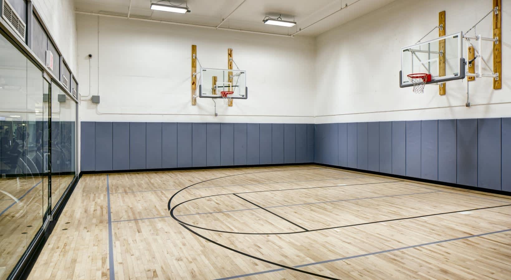 Indoor basketball court with wooden floor, blue wall padding, and three mounted basketball hoops.