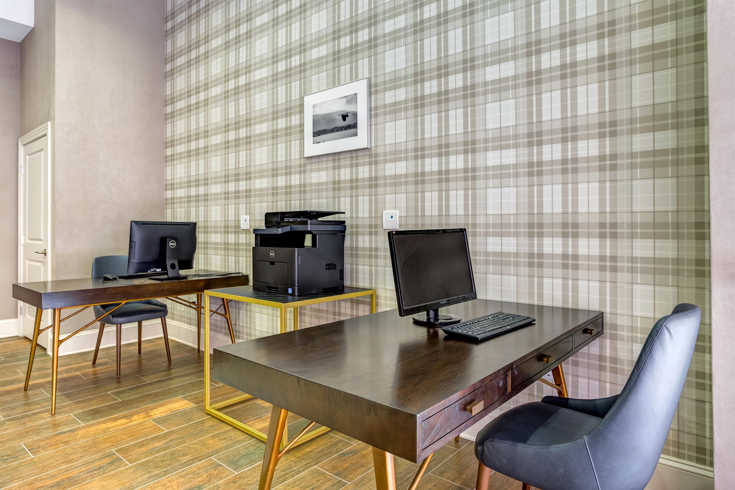 Business center with two desks, computer monitors, printer, and black office chairs against plaid wallpaper.