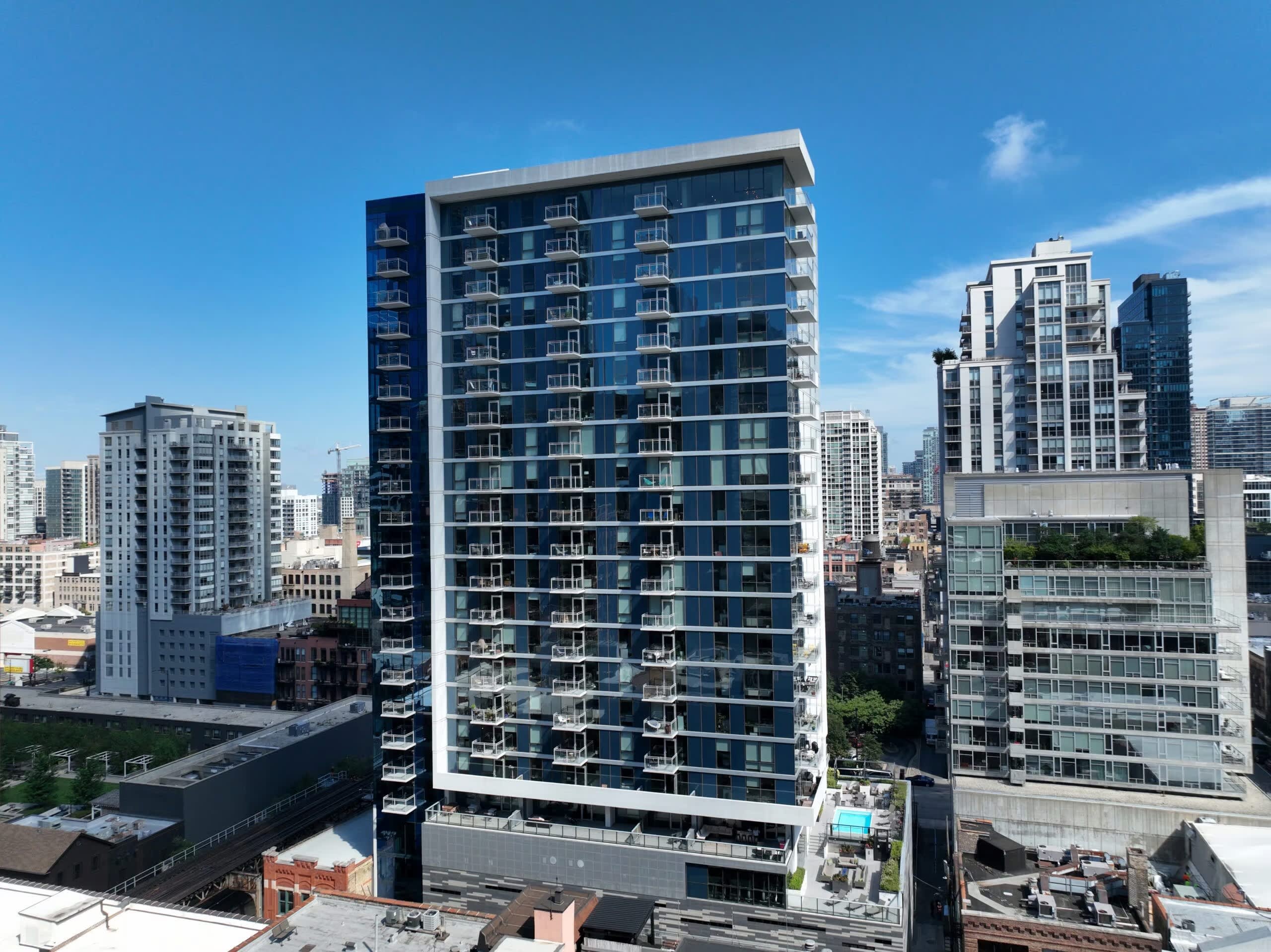 Modern high-rise residential building with dark blue facade, balconies, and floor-to-ceiling windows overlooking Chicago cityscape.