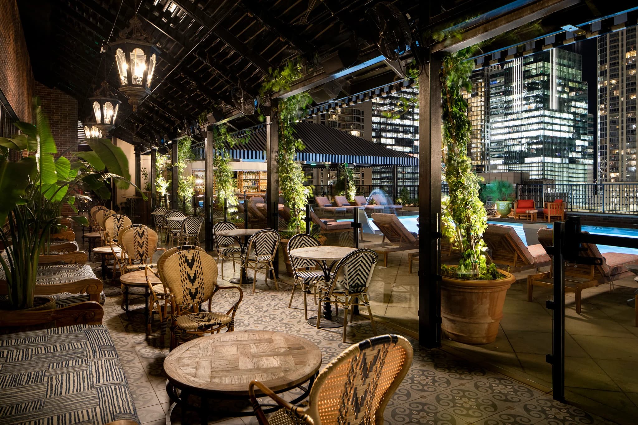 Rooftop lounge with patterned chairs, round tables, climbing ivy on pergola, and downtown Austin skyline at night.