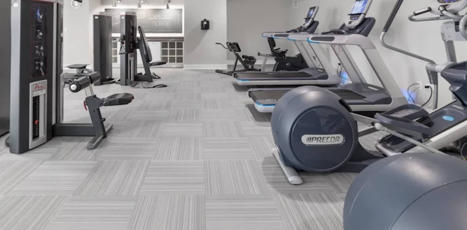 Modern fitness center with treadmills, stationary bikes, exercise equipment, and gray geometric flooring.