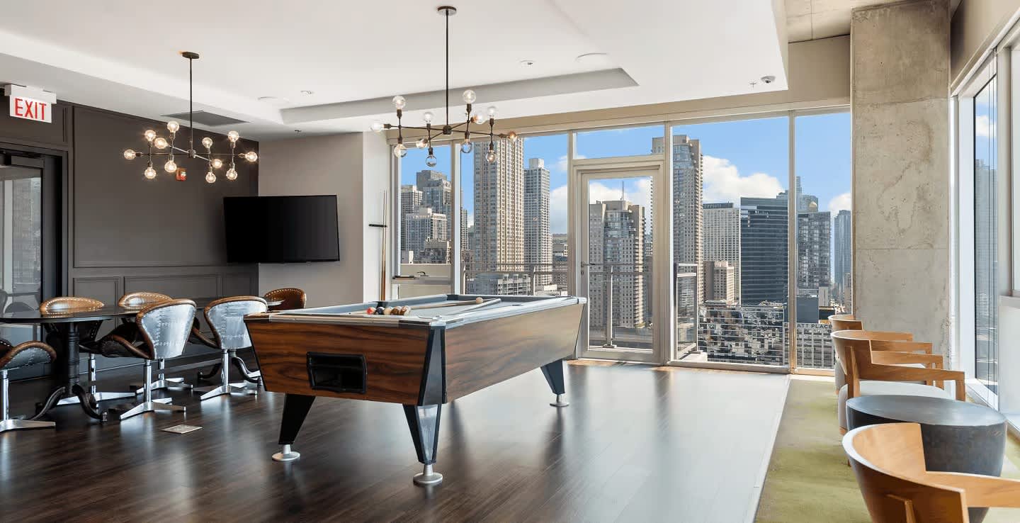 Game room with pool table, pendant lighting, dark wood flooring, and expansive windows with Chicago skyline views.
