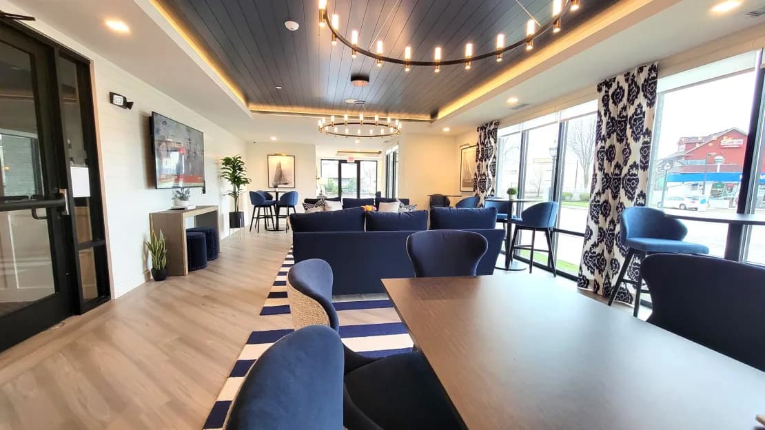 Open common room with navy blue seating, wood flooring, geometric patterned curtains, and recessed ceiling lighting.