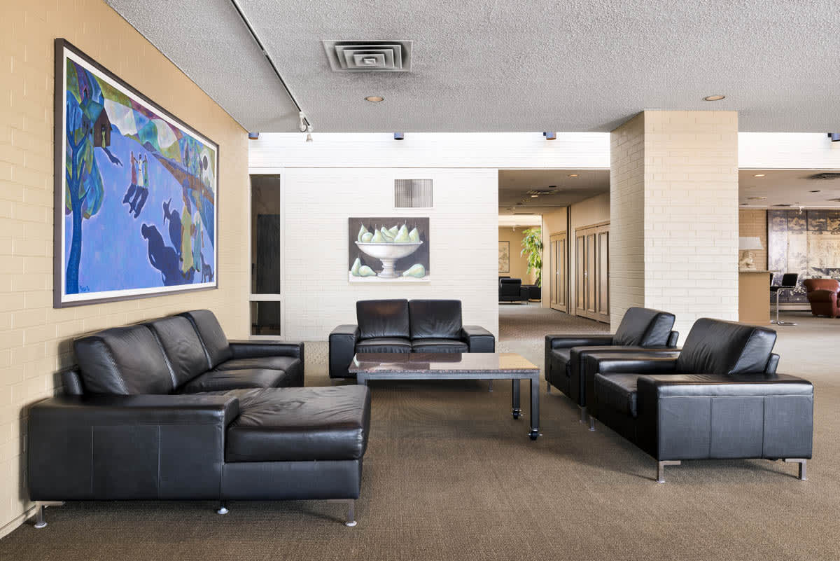 Common lounge area with black leather sofas, wood coffee table, framed blue artwork on cream wall, and recessed lighting.
