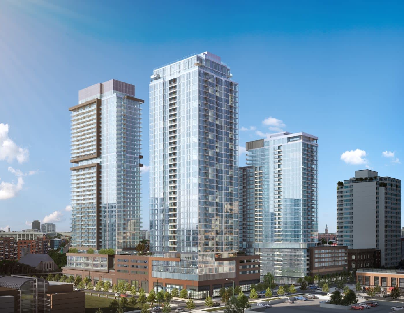 Modern residential high-rise towers with glass and metal facades, ground-level brick buildings, and landscaped plaza in urban setting.