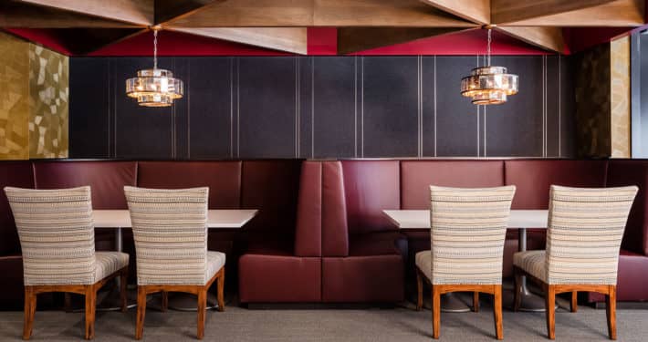 Dining booth with burgundy banquette seating, cream patterned chairs, dark wood-paneled walls, and hanging pendant lights.