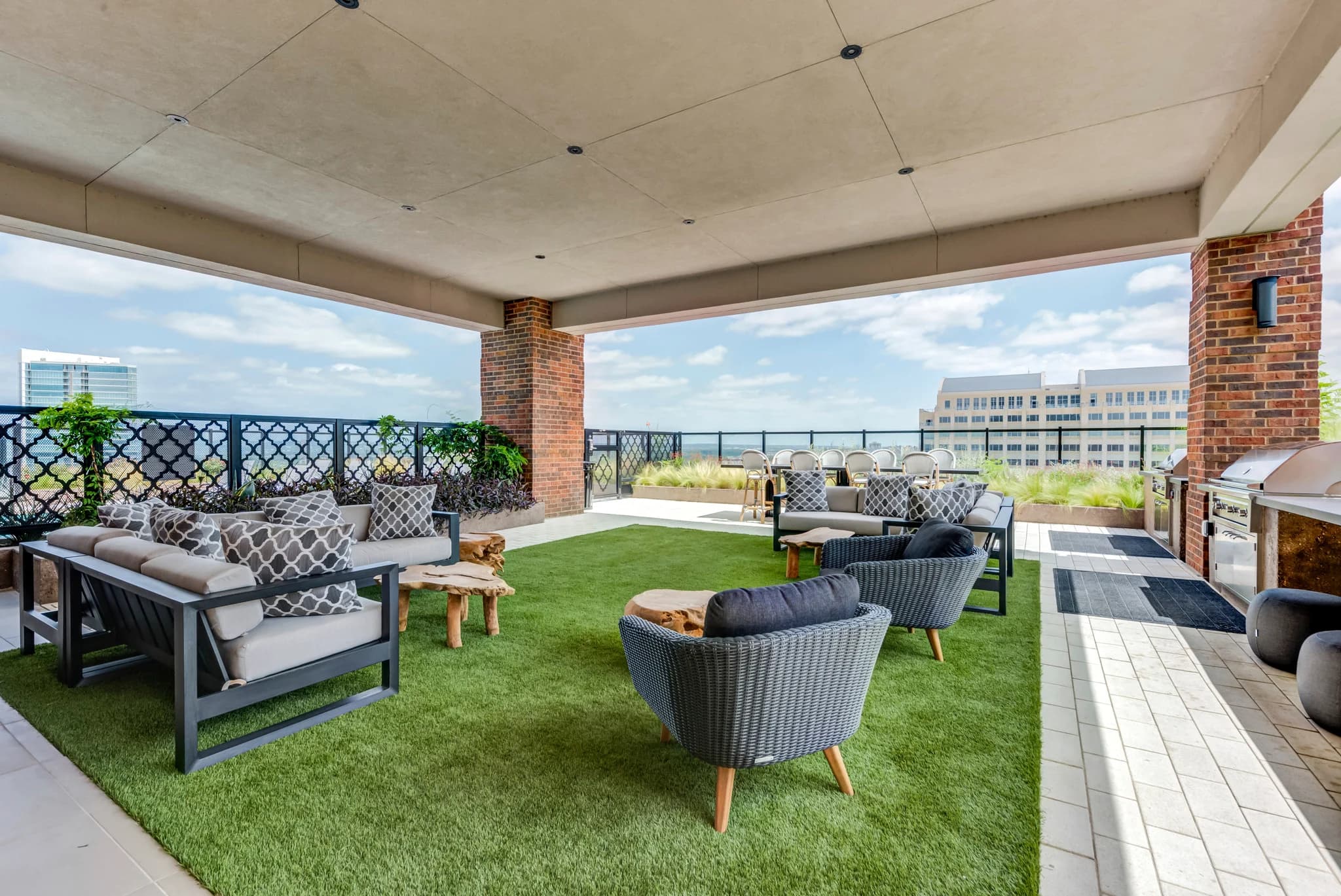 Rooftop terrace with artificial grass, gray wicker lounge chairs, concrete ceiling, brick column, and Austin skyline views.